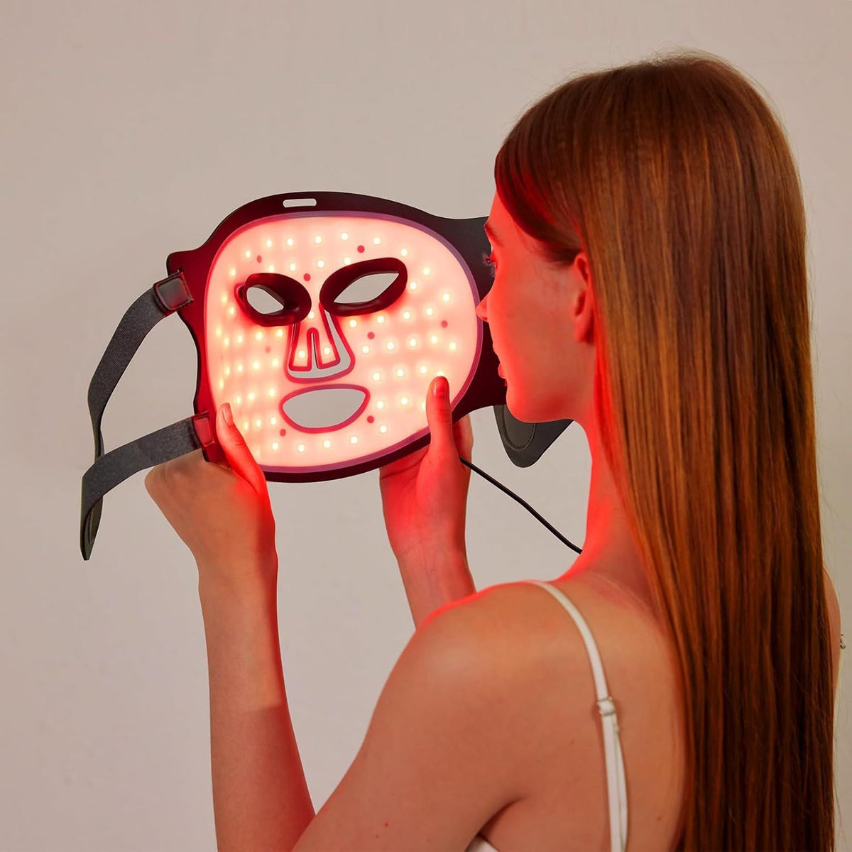 7 Color Rechargeable LED face mask glowing red with multiple LED lights held by a woman with long hair