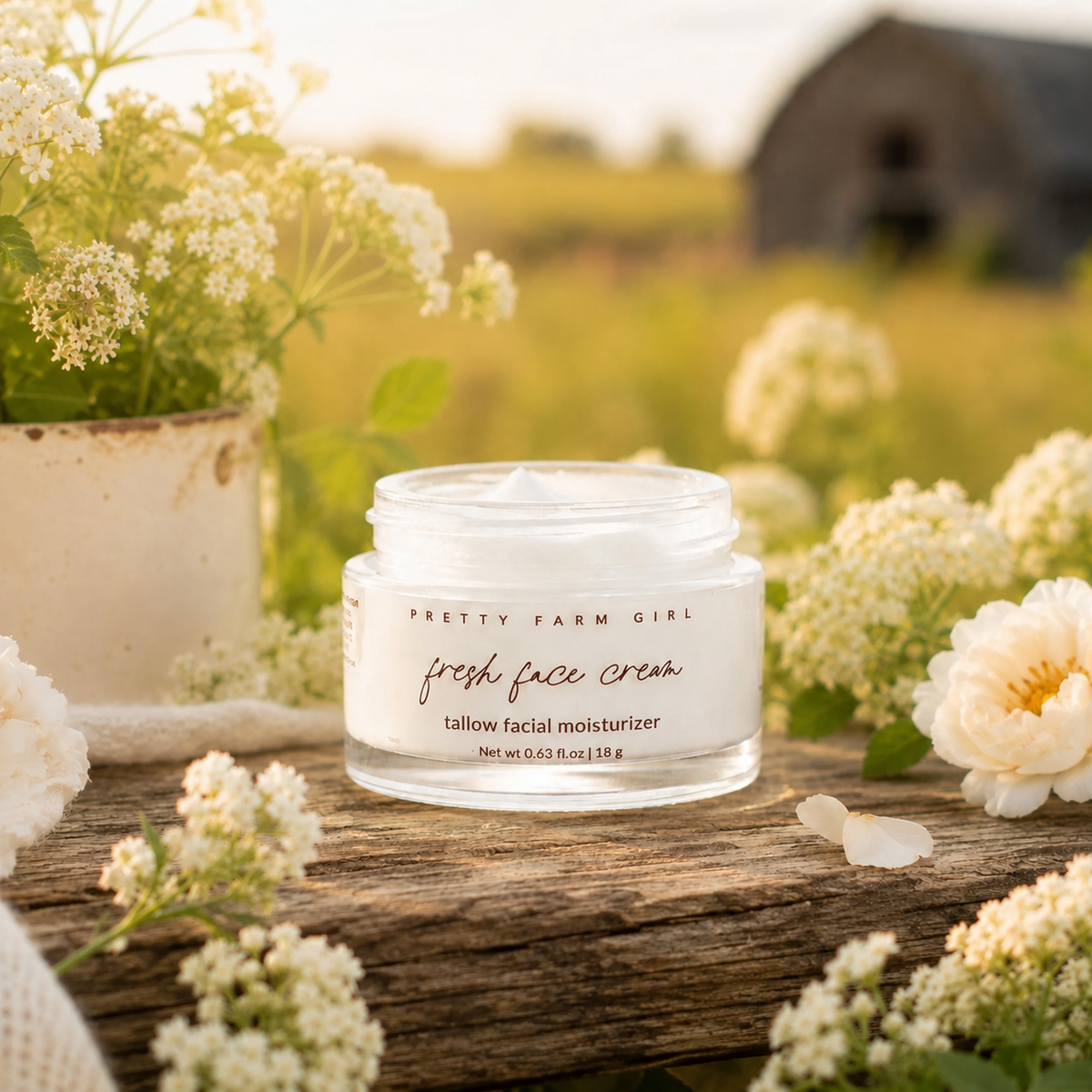 Glass jar of Anti-Aging Grass-Fed Tallow white face cream with black text label, natural floral accents and soft cream texture visible.