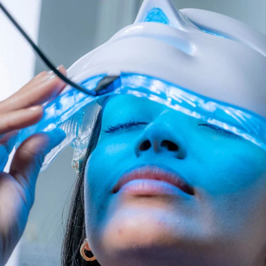 Light Therapy LED Face Mask glowing blue on face with adjustable fit and flexible clear edges, worn by person with eyes closed