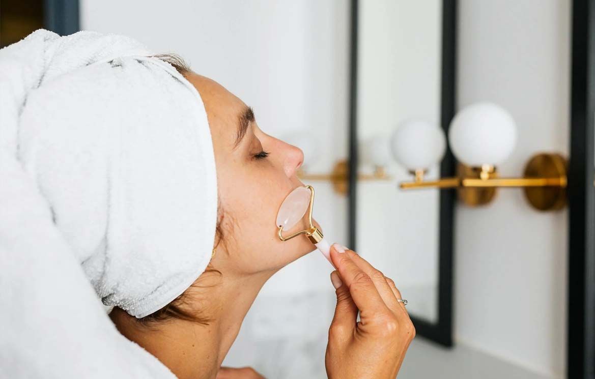 Rose Quartz Facial Roller being used on woman's cheek with towel wrapped around her head in a skincare routine