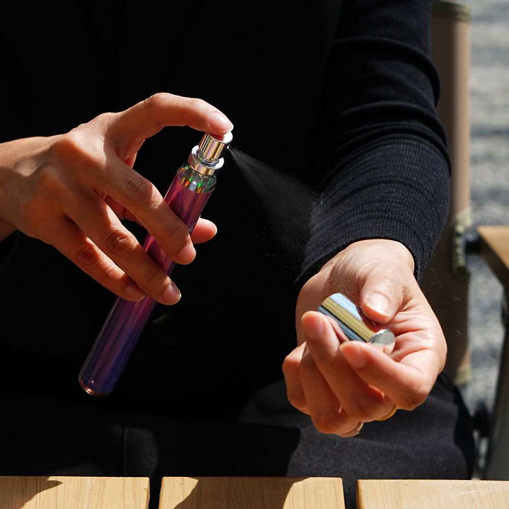 Women's Eau De Parfum spray in a sleek, iridescent purple travel bottle being applied to the wrist, portable and elegant